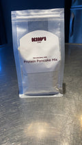 A clear stand-up pouch of Kiwi Cafe Protein Pancake Mix sitting on a brushed metal countertop.