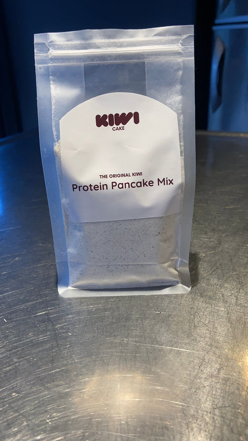 A clear stand-up pouch of Kiwi Cafe Protein Pancake Mix sitting on a brushed metal countertop.